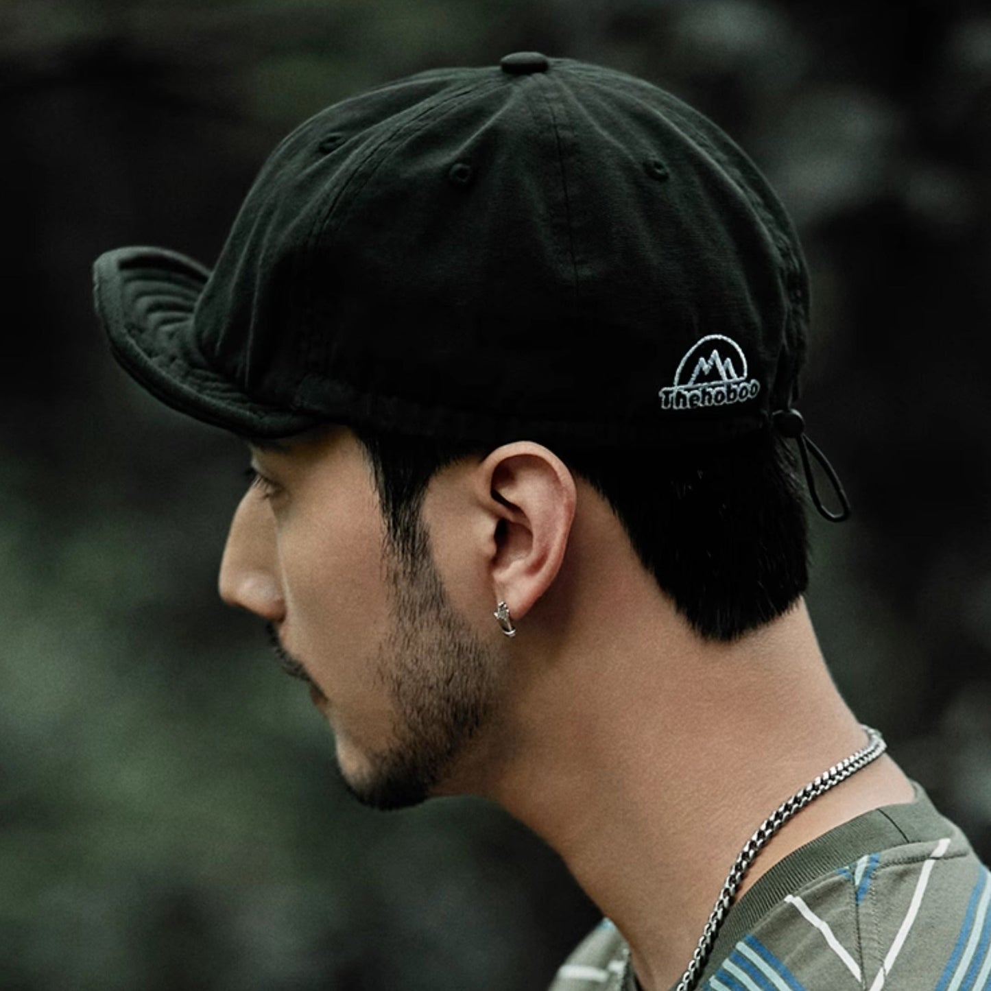 Man wearing a black cap with a logo, looking to the side with a blurred natural background