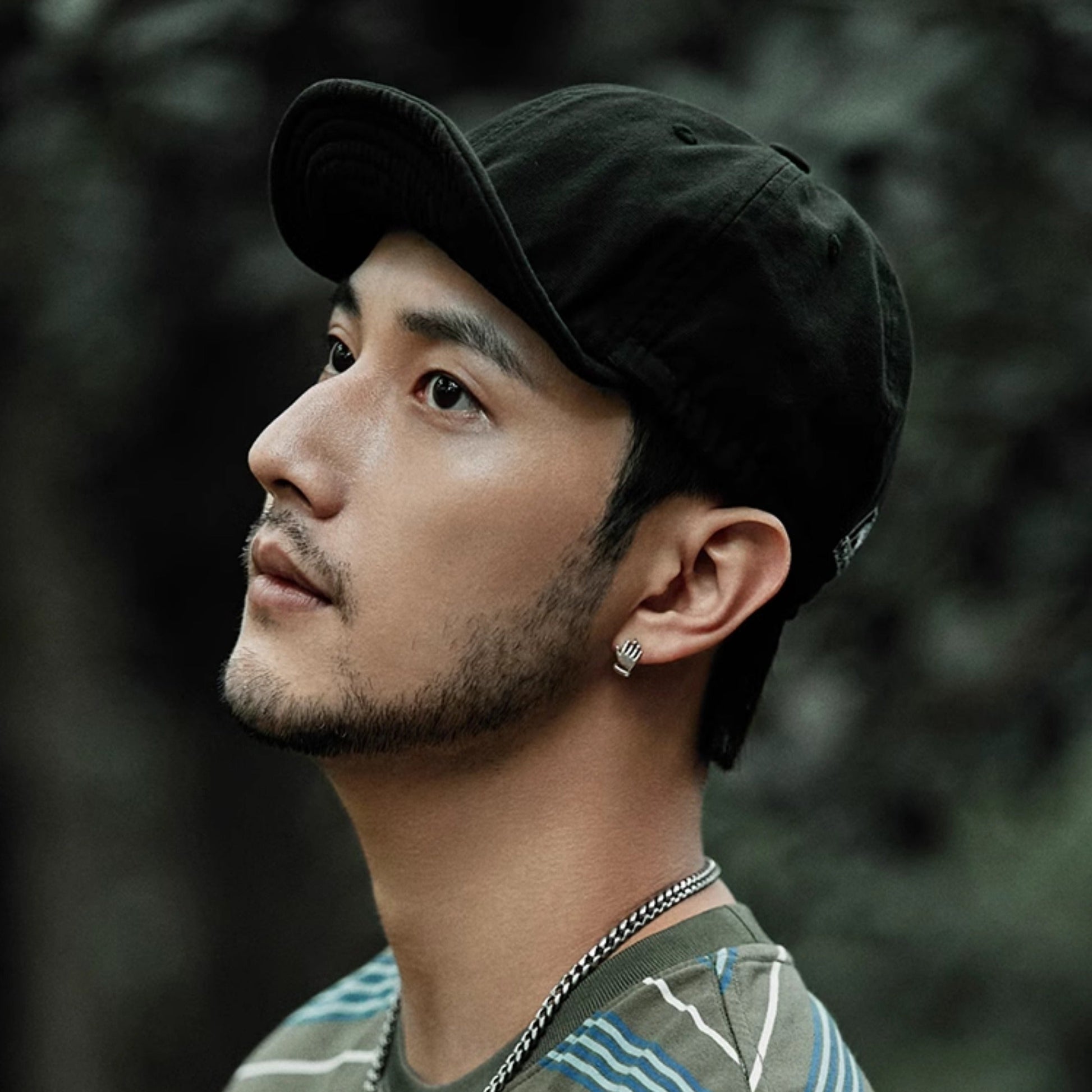 Man wearing a black cap and striped shirt with a blurred natural background