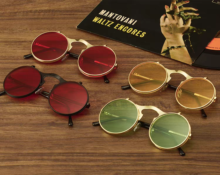Four pairs of round sunglasses in red, gold, and green on a wooden surface