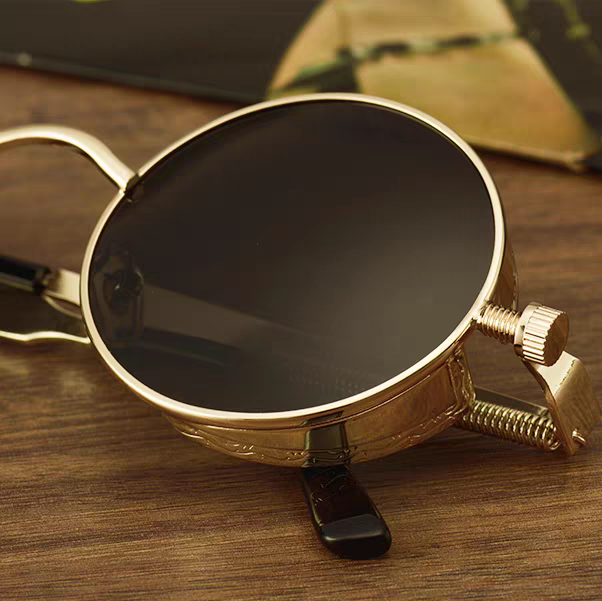 Gold-framed sunglasses with a black lens on a wooden surface