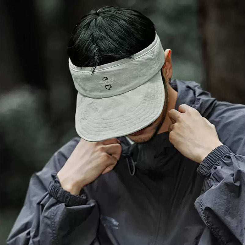 Person wearing a beige visor and dark jacket in a forest setting
