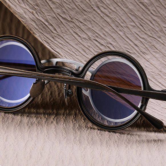 Round sunglasses with black frame and blue lenses on a wooden surface.