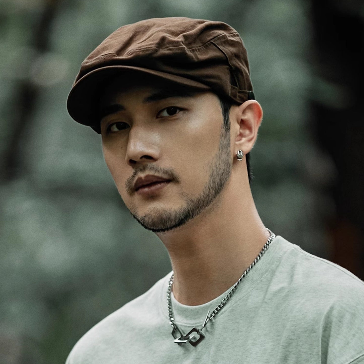 Man wearing a brown cap and light green shirt with a blurred natural background