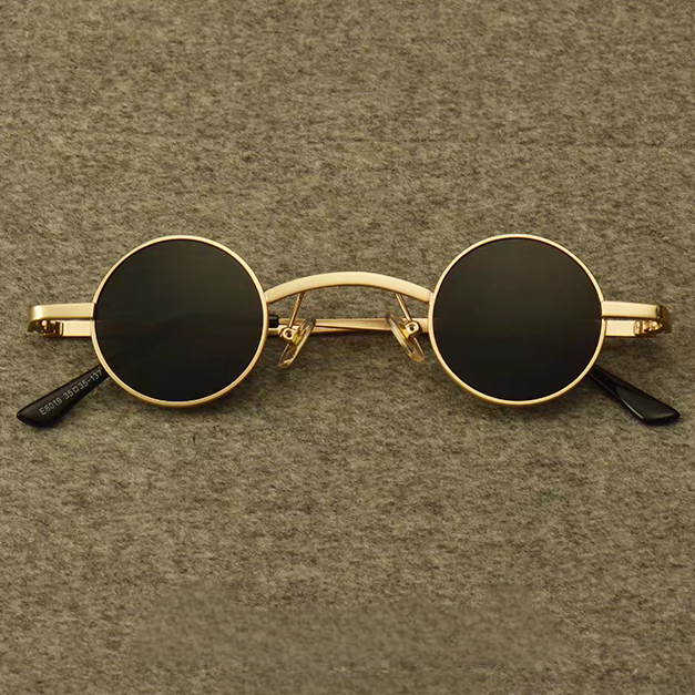 Small round sunglasses with gold frame and black lenses on a brown textured background