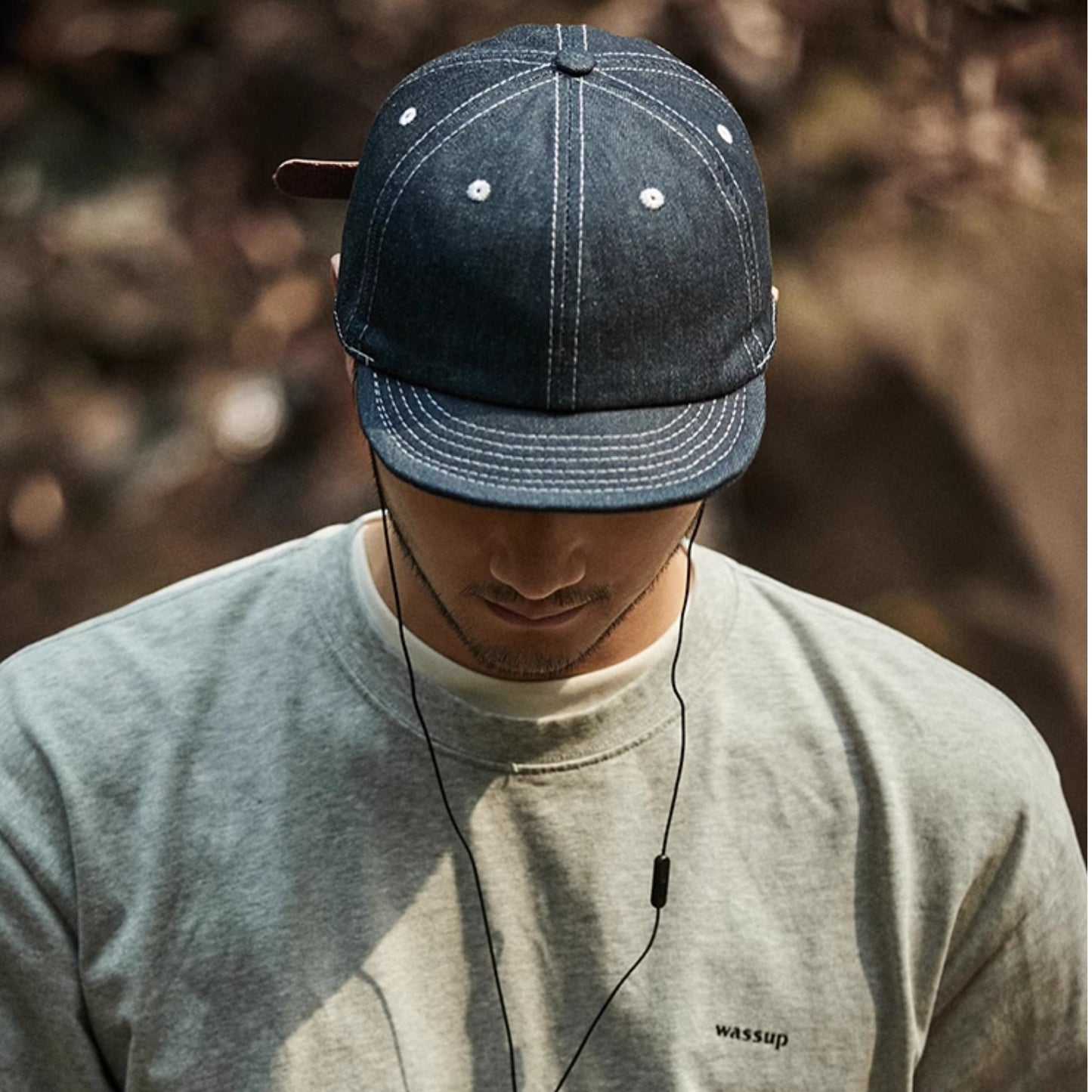Person wearing a denim cap and listening to music with earphones, blurred natural background