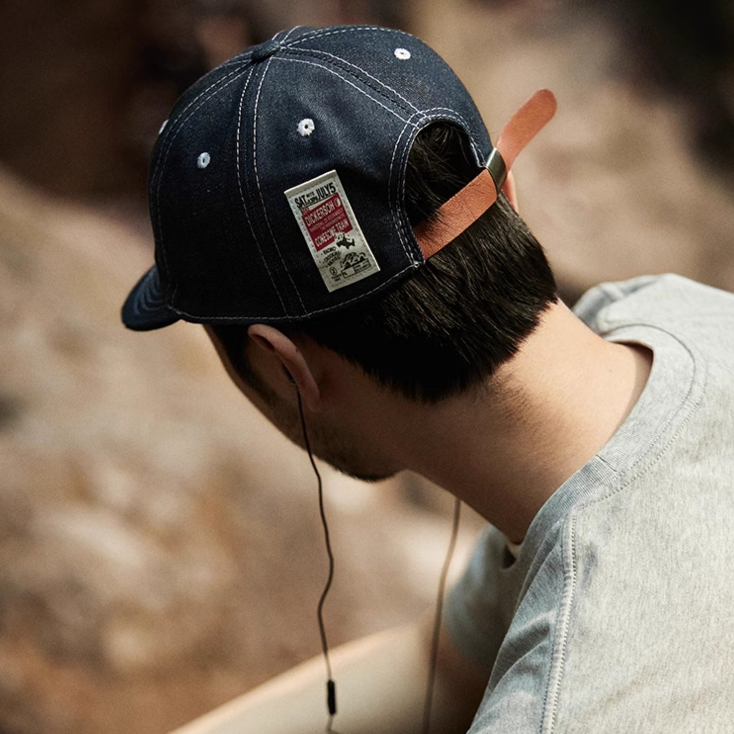 Person wearing a dark blue cap with a patch, sitting outdoors.