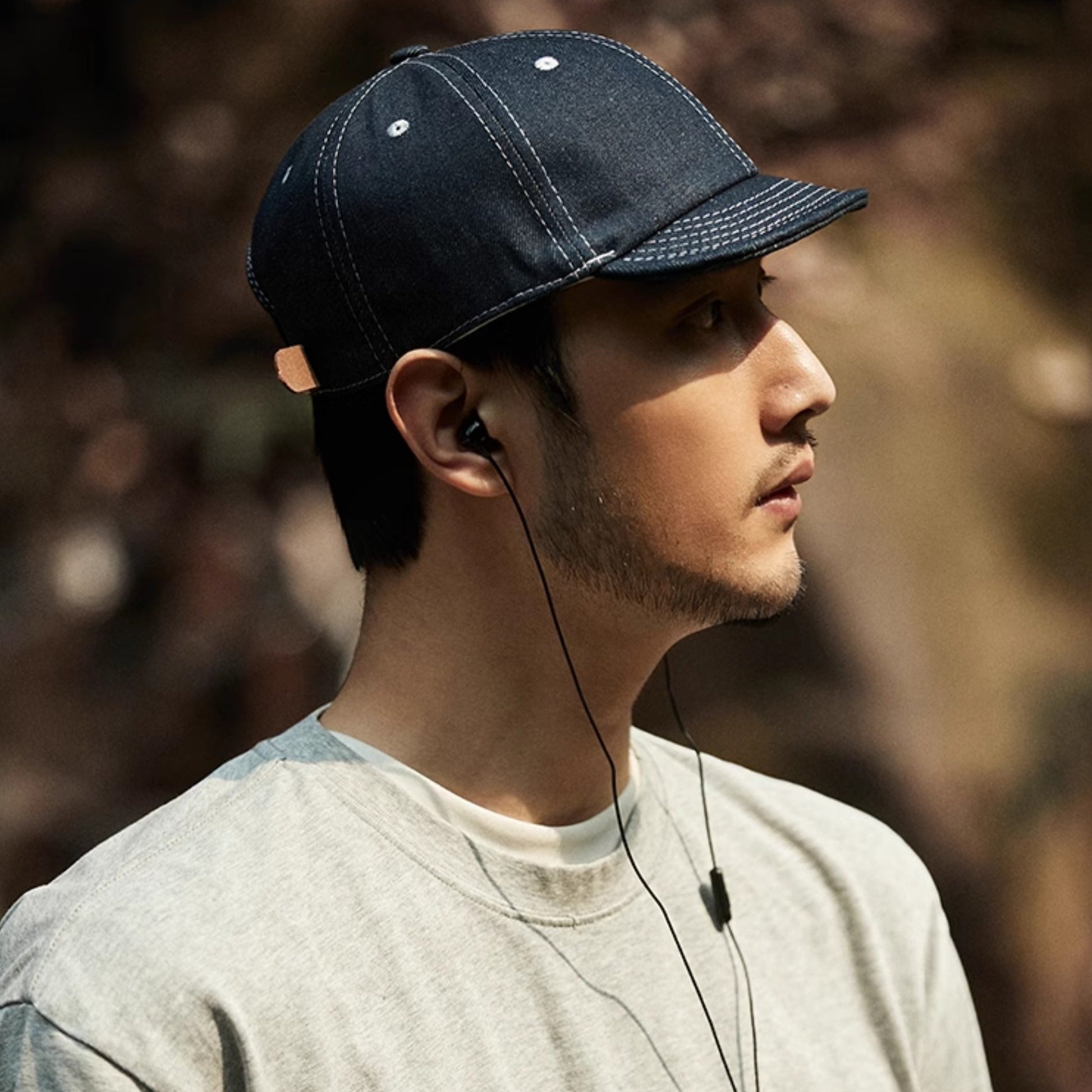 Man wearing a dark blue cap and listening to music with earphones, standing outdoors.