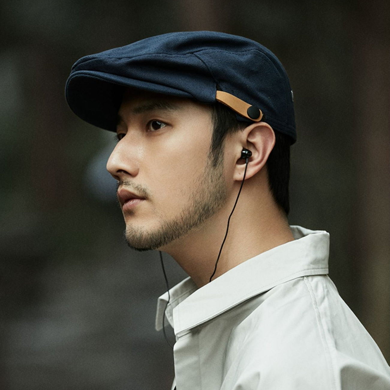 Man wearing a navy cap and white shirt with earphones, against a dark background