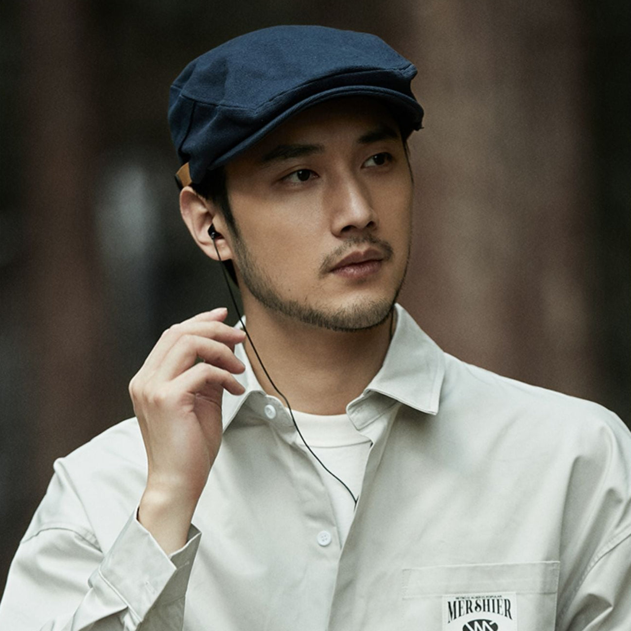 Man wearing a cap and light-colored shirt with a brand logo, against a blurred background