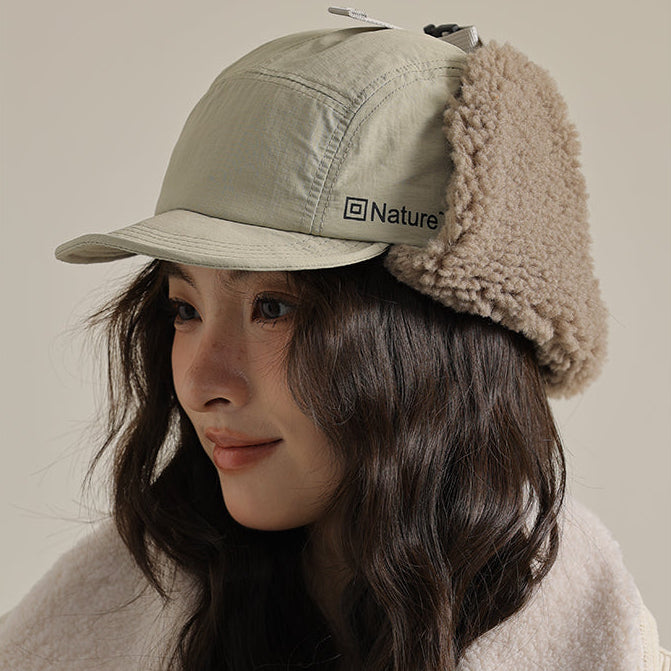 Person wearing a beige winter cap with fur trim and a matching jacket, with 'Nature' logo.