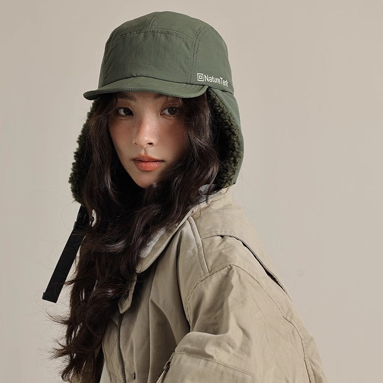 Person wearing a green hooded cap and beige jacket on a plain background