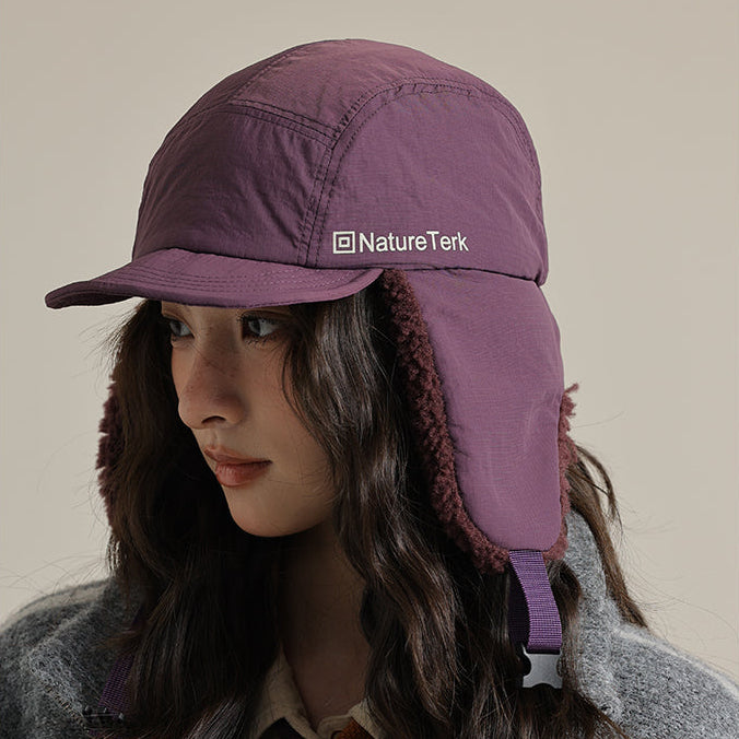 Person wearing a purple winter cap with ear flaps on a beige background