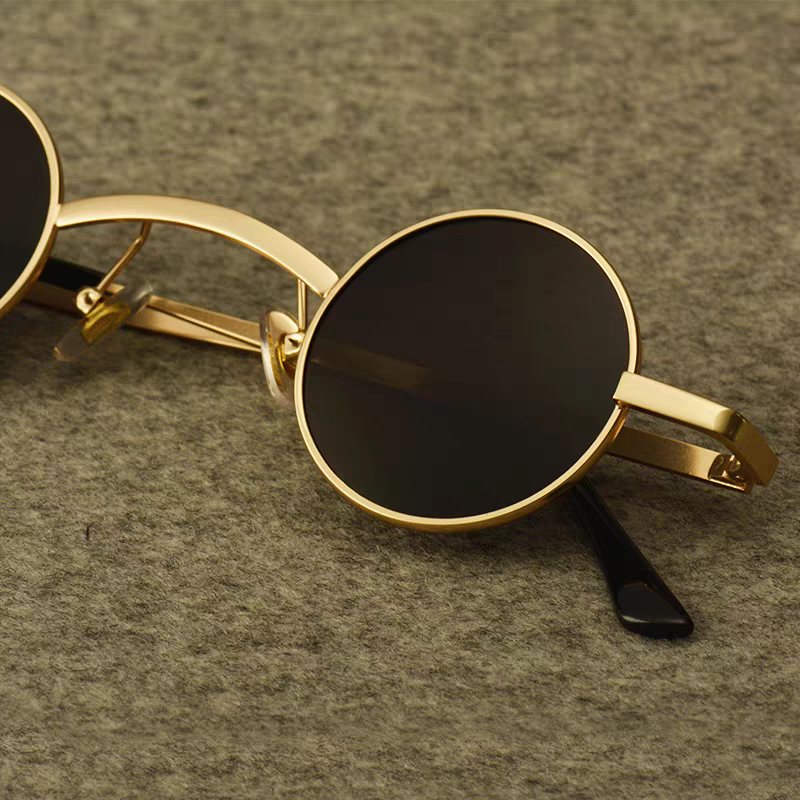 Round sunglasses with gold frame and black lenses on a textured gray surface