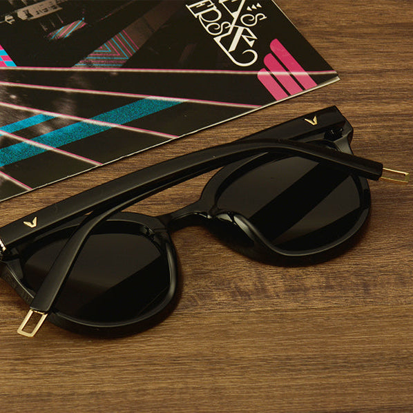 Black sunglasses with gold accents on a wooden surface with a colorful album cover.
