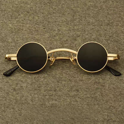 Small round sunglasses with gold frame and black lenses on a brown textured background