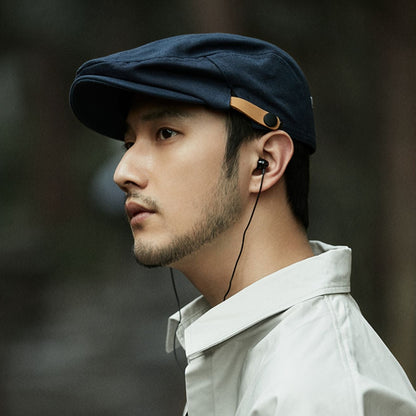 Man wearing a navy cap and white shirt with earphones, against a dark background